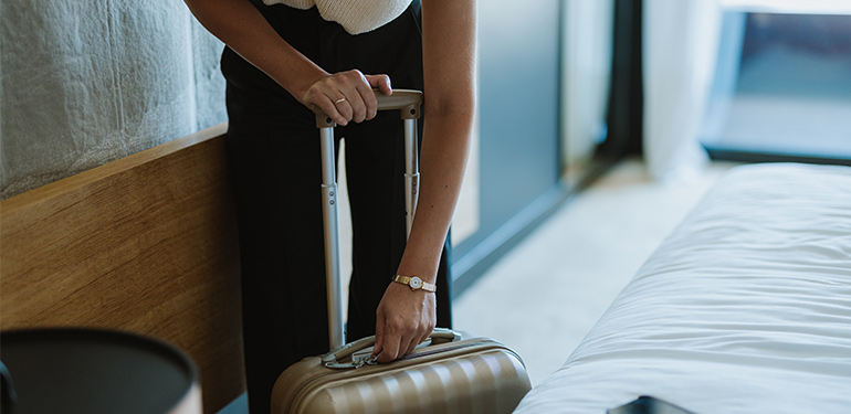 Kvinna böjer sig ner för att öppna sin resväska i ett hotellrum