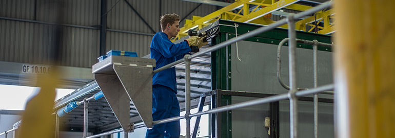 Man i blå arbetskläder borrar inne i en industrilokal