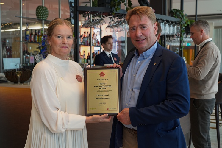Två personer som håller upp ett certifikat som avser Väl brandskyddat hotell