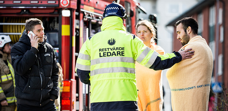 Restvärdeledare pratar med skadedrabbade, brandbil i bakgrunden