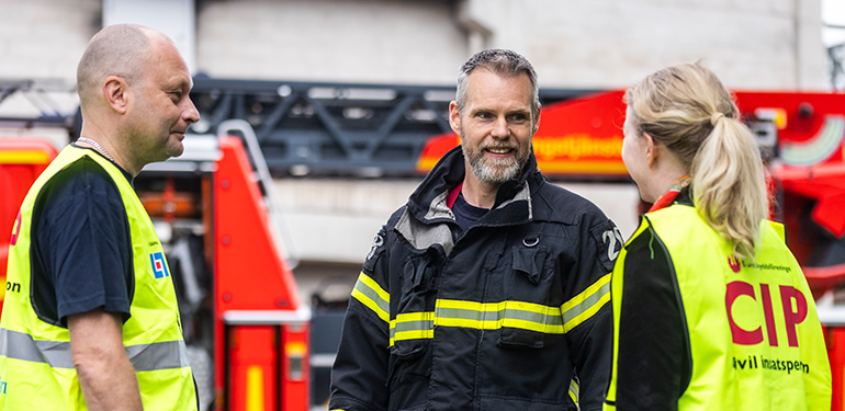 Man från räddningstjänsten pratar med två civila insatspersoner
