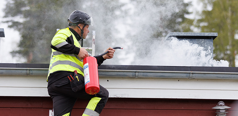 Man på en stege riktar brandsläckare mot rök på yttertak