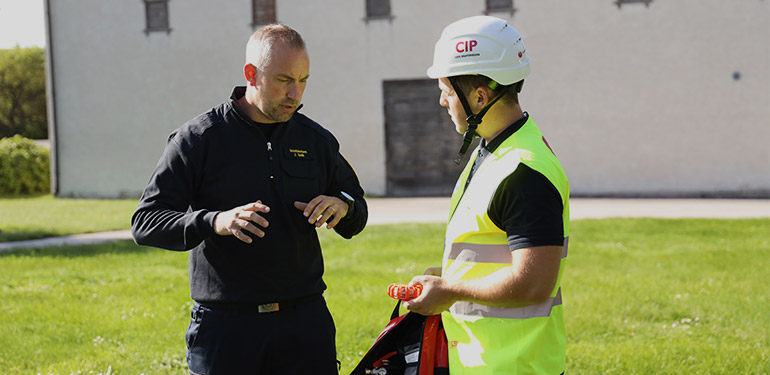 Man från räddningstjänsten står på en gräsmatta och pratar med en civil insatsperson