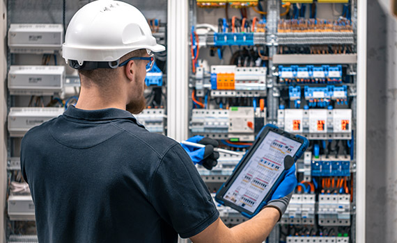 Man i hjälm utför kontroll på elanläggning
