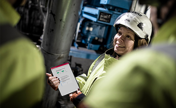 Kvinna med arbetskläder i industriell miljö håller i surfplatta