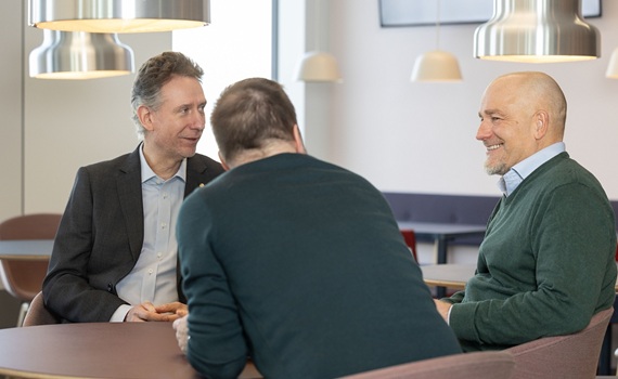 Tre personer som sitter vid ett bord och samtalar.