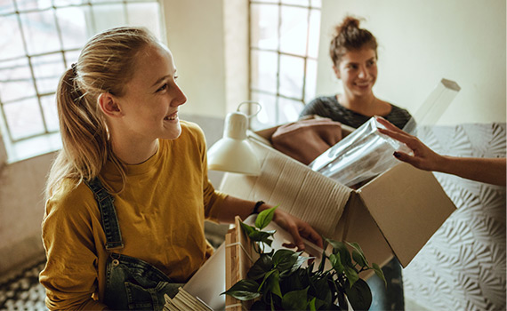 Två unga tjejer bär på flyttkartonger i en trappuppgång