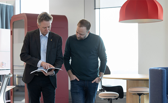 Två män kollar ner i en bok och diskuterar något