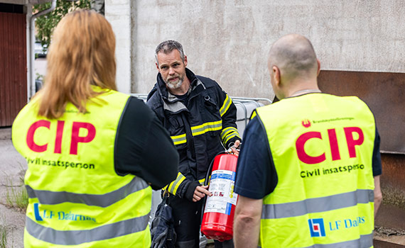 Man från räddningstjänsten visar två civila insatspersoner en brandsläckare