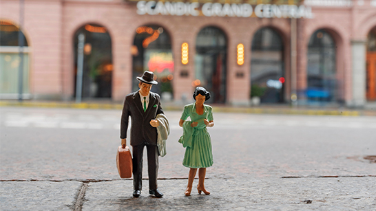 Två små leksaksfigurer som föreställer en man och en kvinna, uppställda på gatan framför Scandic Grand Central