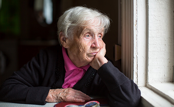 Äldre kvinna som ser ut genom fönstret