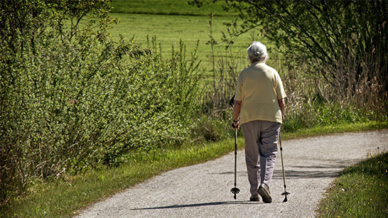 Äldre person med gångstavar på en gångväg