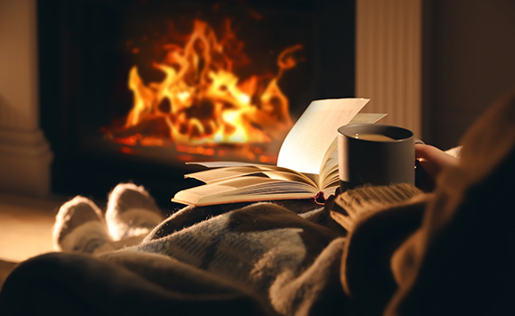 Kvinna dricker te och läser bok framför eldstad