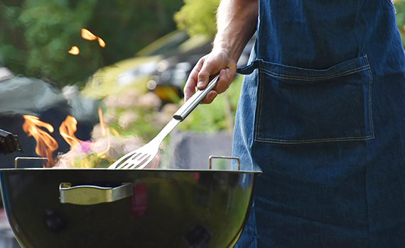 Person står vid en grill och håller i en stekspade