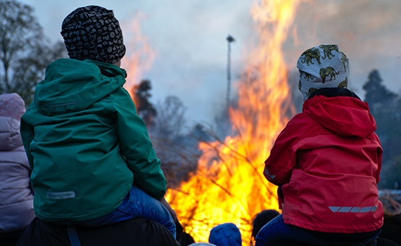Två barn sitter på sina föräldrars axlar och kollar på majbrasa