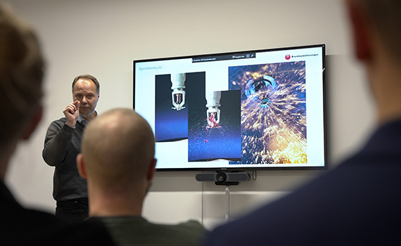 Föreläsare står vid en tv-skärm och presenterar