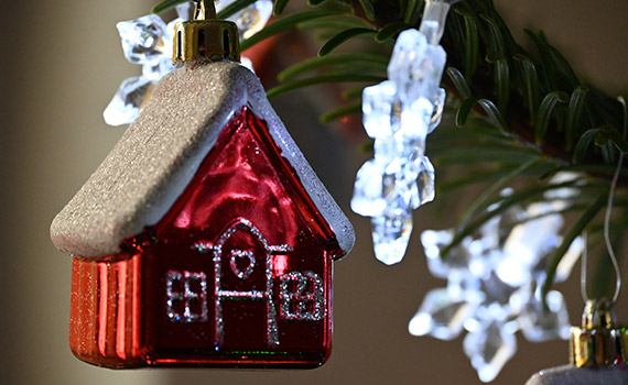 Ett julpynt i form av ett litet rött hus hänger i en julgran inomhus