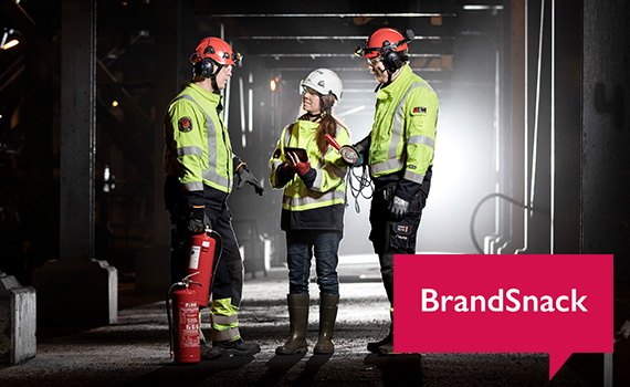 Två män och en kvinna i gula arbetskläder står och diskuterar något nere i en mörk gruva