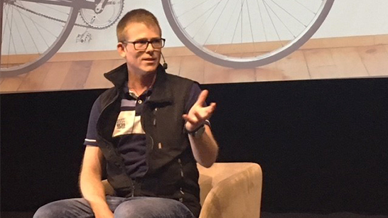 Björn Almberger sitter i en fotöljd och pratar mot publiken