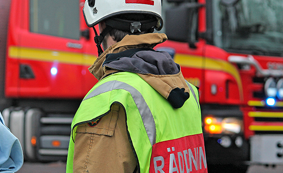 En person från Räddningstjänsten står med ryggen vänd mot kameran och en brandbil skymtas i bakgrunden