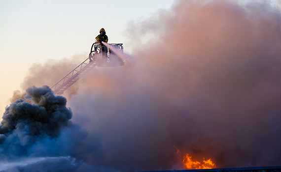 Brandman står på en stege och sprutar vatten mot en brand