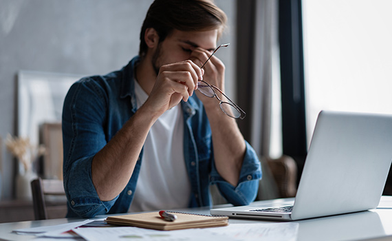 Oroad man sitter vid ett bord med dator och papper