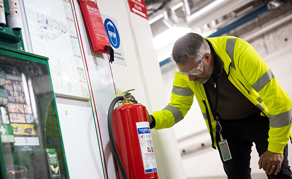 Man i gula arbetskläder i industrilokal kontrollerar en brandsläckare