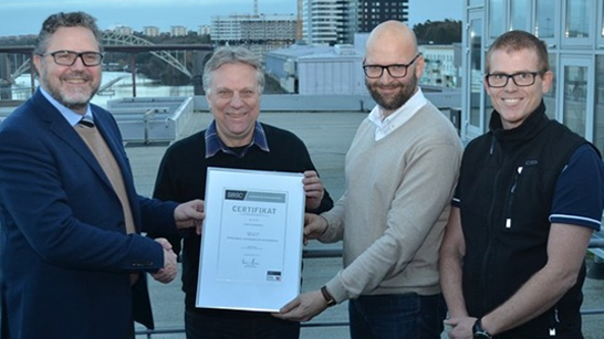 Anders Reinholdsson står bredvid tre andra personer och tar emot ett inramat certifikat