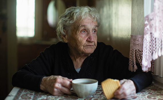 Äldre kvinna håller i en kaffekopp och kollar ut genom fönstret