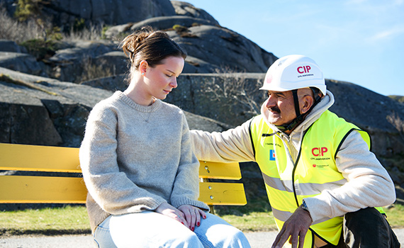 Ung tjej sitter på en bänk och ser nedstämd ut, får stöd av Civil insatsperson som står på huk bredvid