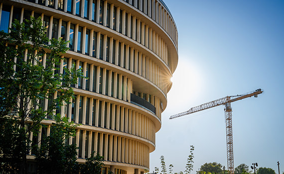 Rund kontorsbyggnad mot molnfri himmel med byggkran i bakgrunden